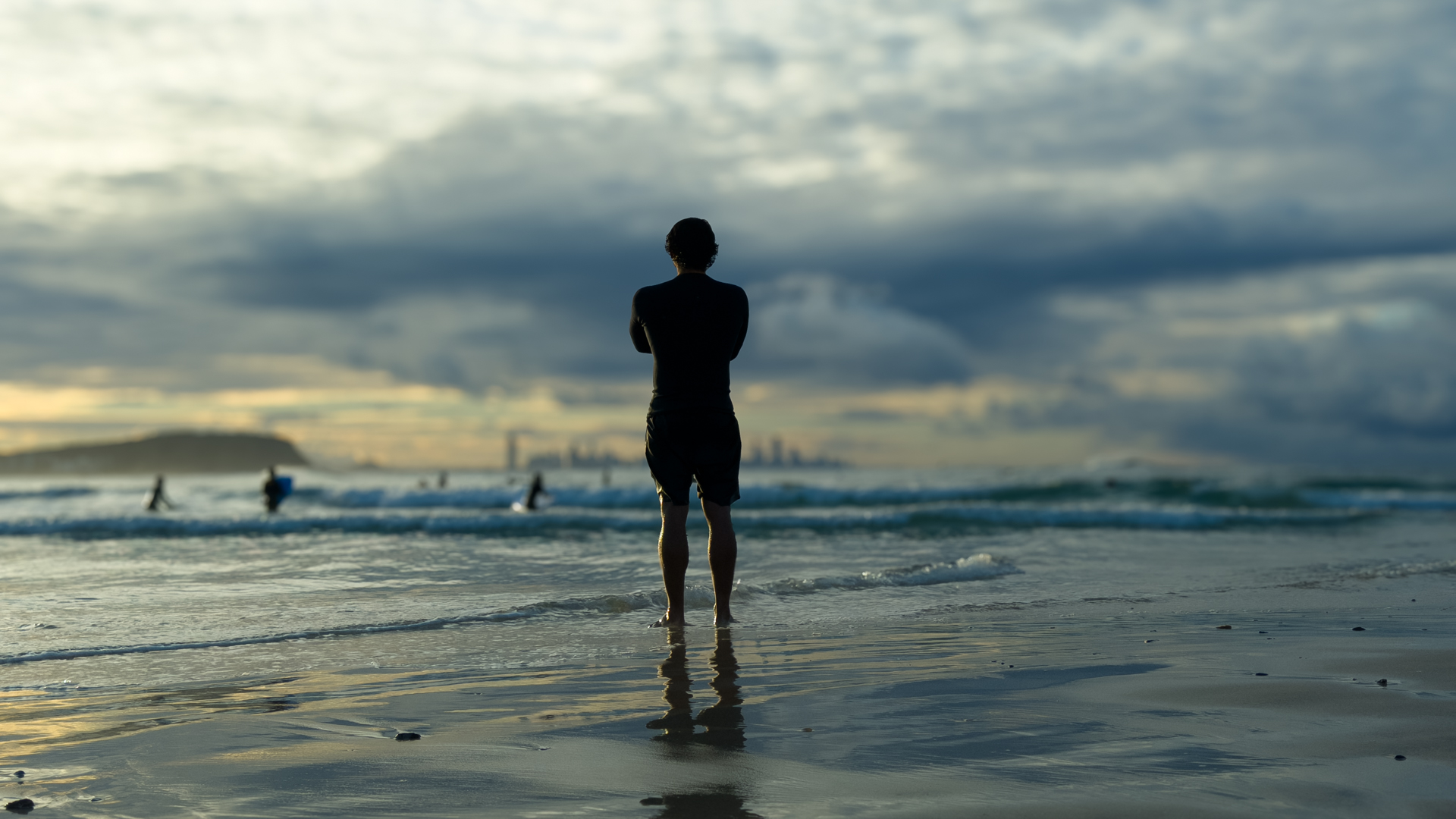 A figure at the water's edge at Currumbin at last light, the Gold Coast skyline on the horizon and a reflection in the wet sand.