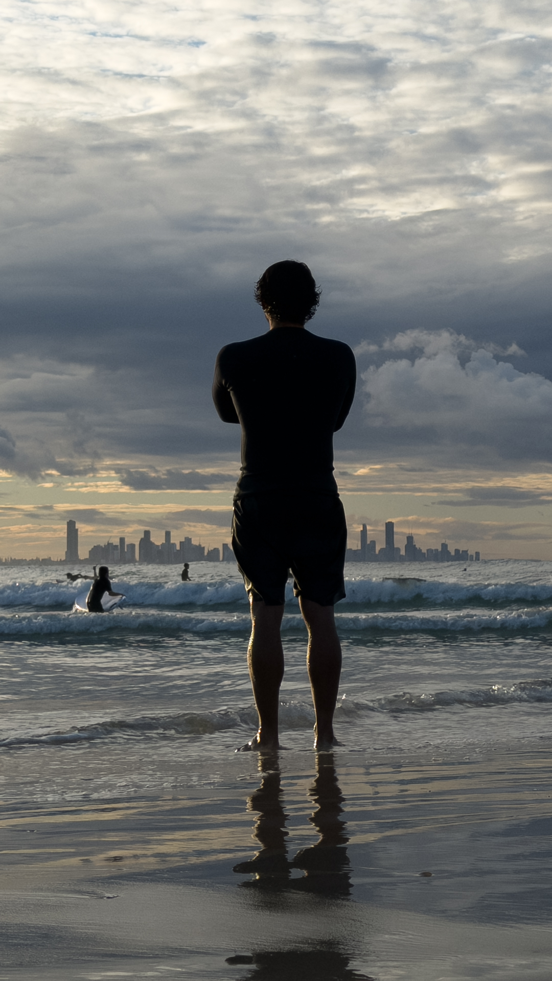 A figure at the water's edge at Currumbin, the Gold Coast skyline on the horizon.