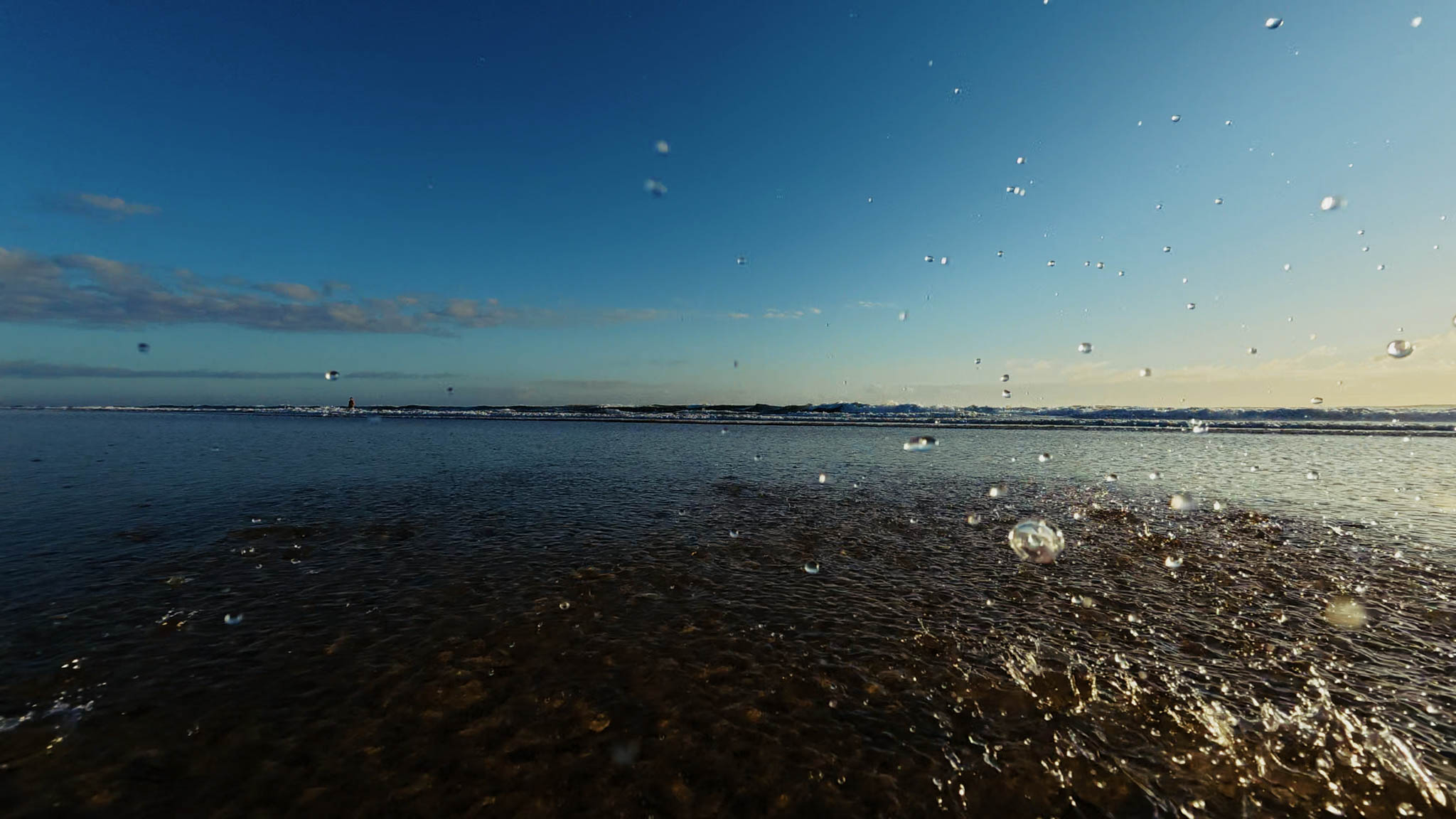 Sea spray suspended over a calm shoreline at sunset